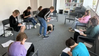 Mokiniai ir suaugusieji psichologo užsiėmime pildo užduočių lapus