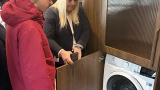 Viešbučio darbuotoja rodo mokiniui skalbimo mašiną kambaryje